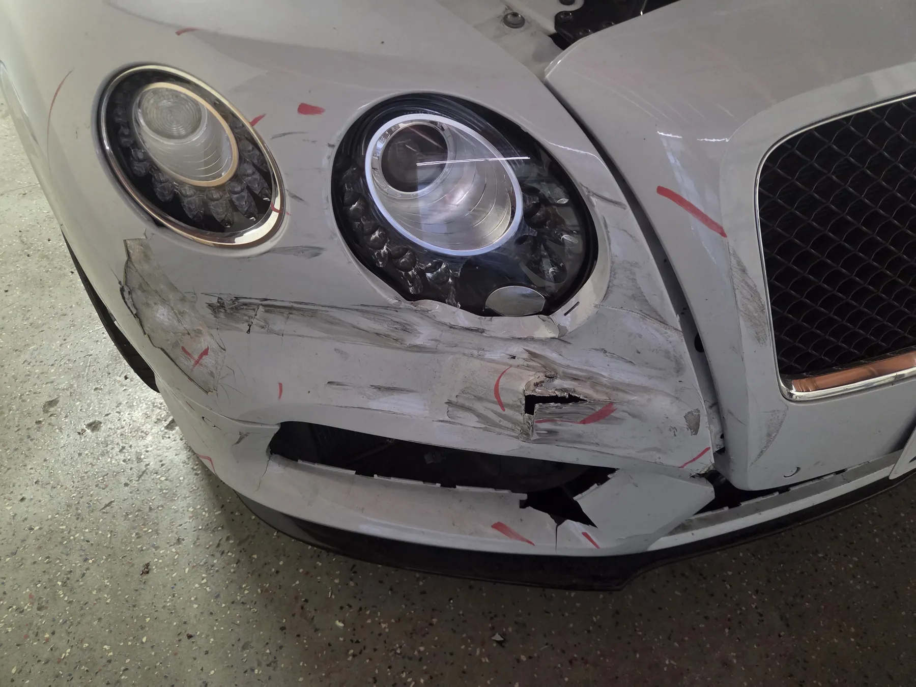White Bentley front bumper with cracks, scrapes, and collision damage before repair
