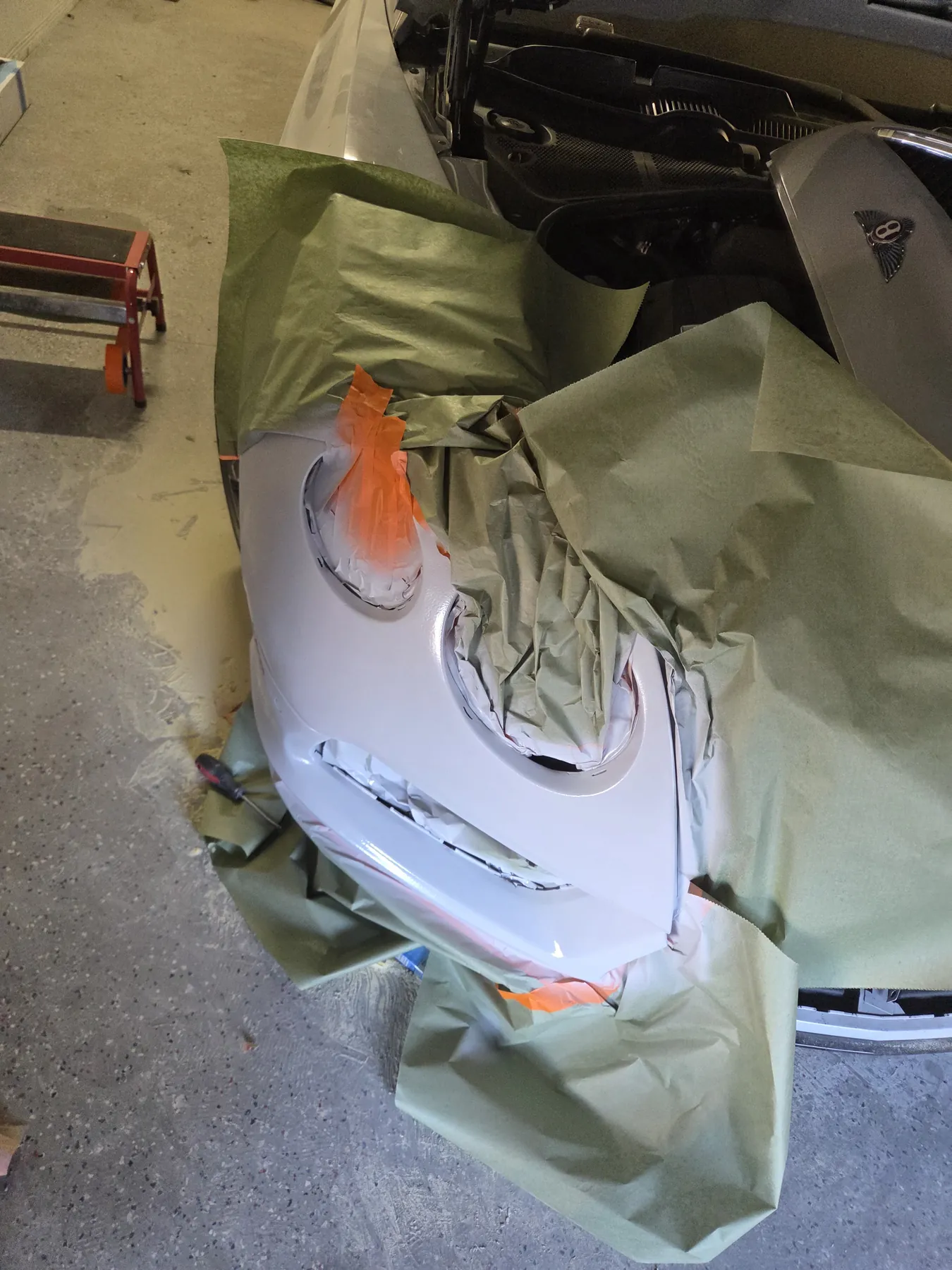 White Bentley front bumper masked during refinishing preparation