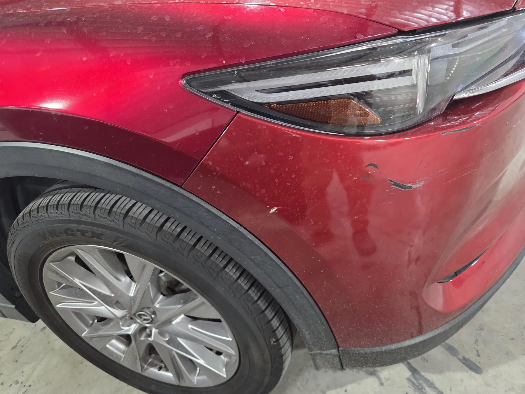 Red Mazda front bumper with scrapes and paint damage before repair